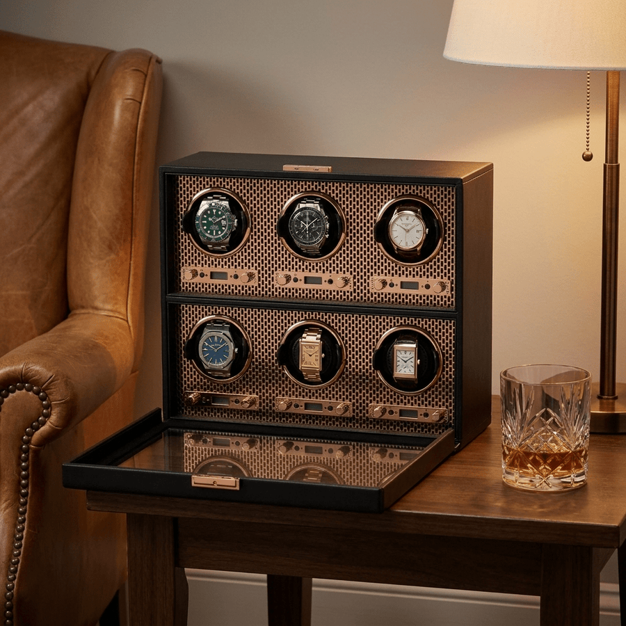 Wolf 1834 Axis watch winder voor 6 horloges in koperen (copper) afwerking, gevuld met verschillende luxe horloges, op een bijzettafel naast een leren fauteuil