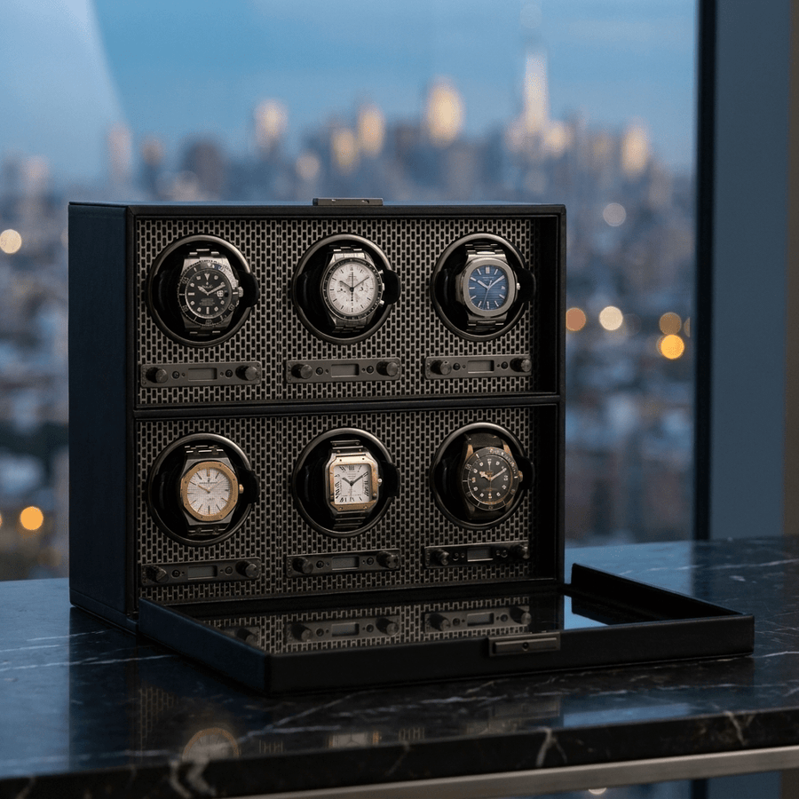 Wolf 1834 Axis watch winder voor 6 horloges in powder coat (mat zwart) afwerking, gevuld met verschillende luxe horloges, op donker marmer met een avondlijke skyline op de achtergrond