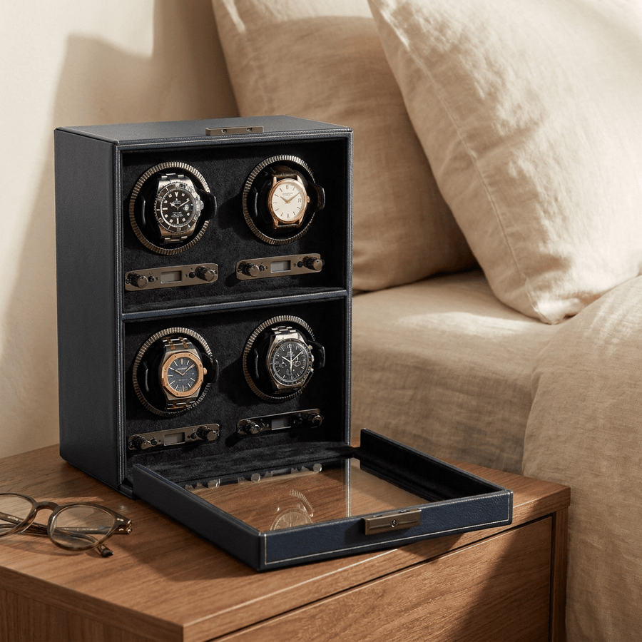 Wolf 1834 British Racing watch winder voor 4 horloges in saphire black (zwart leer), gevuld met verschillende luxe horloges, op een nachtkastje